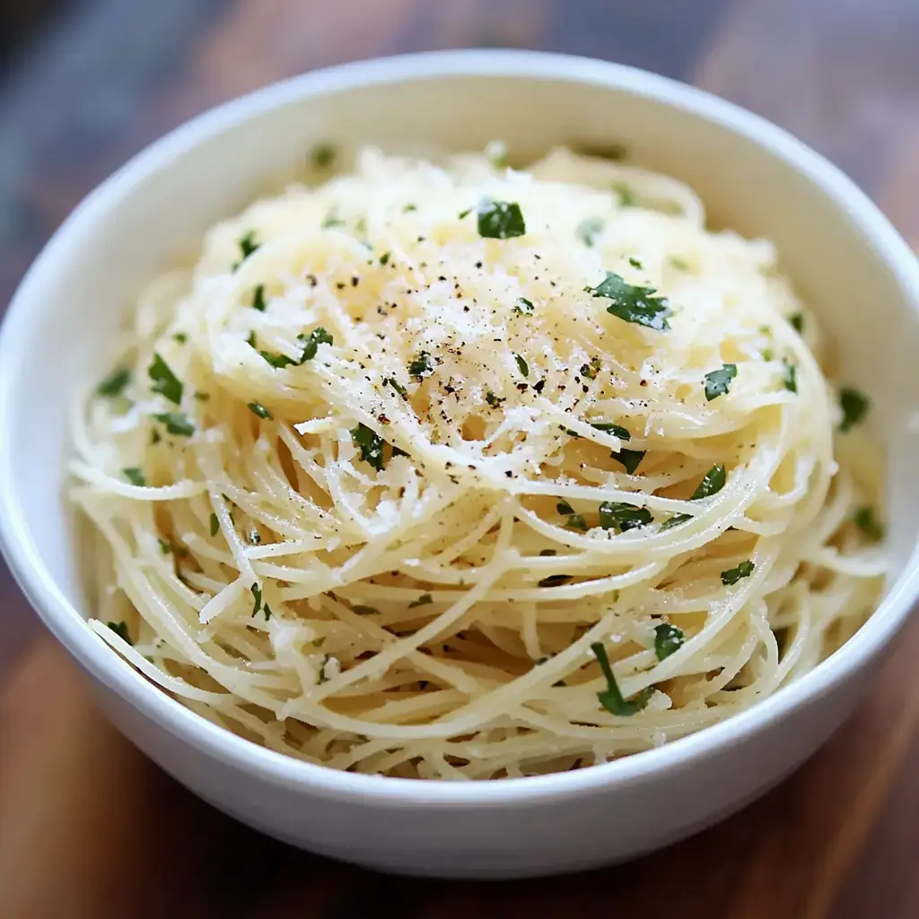 A bowl of spaghetti topped with grated cheese and fresh herbs, sprinkled with black pepper.