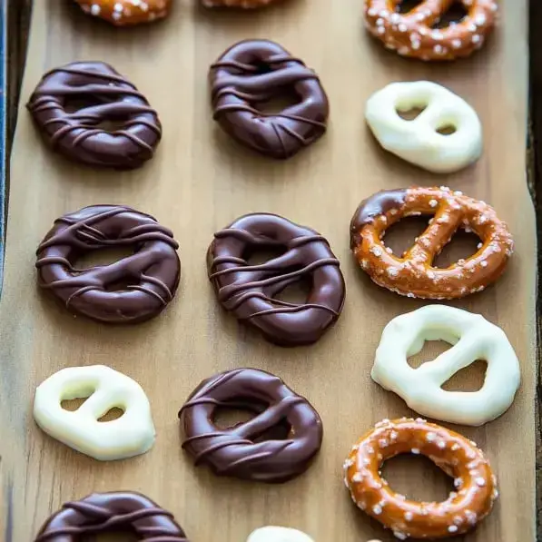 A wooden platter is filled with chocolate-covered pretzels and regular pretzels in various arrangements.