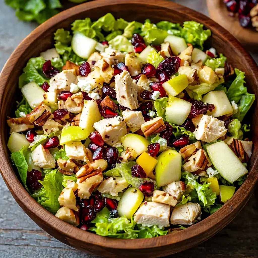 A colorful salad bowl filled with mixed greens, diced chicken, apples, pomegranate seeds, dried cranberries, and nuts.