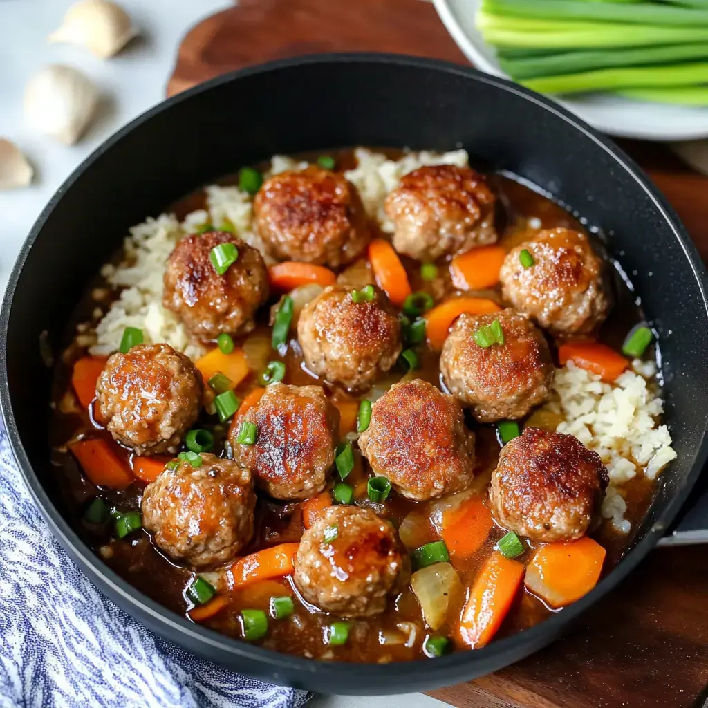 A skillet filled with glazed meatballs, carrots, and green onions served over rice in a savory sauce.