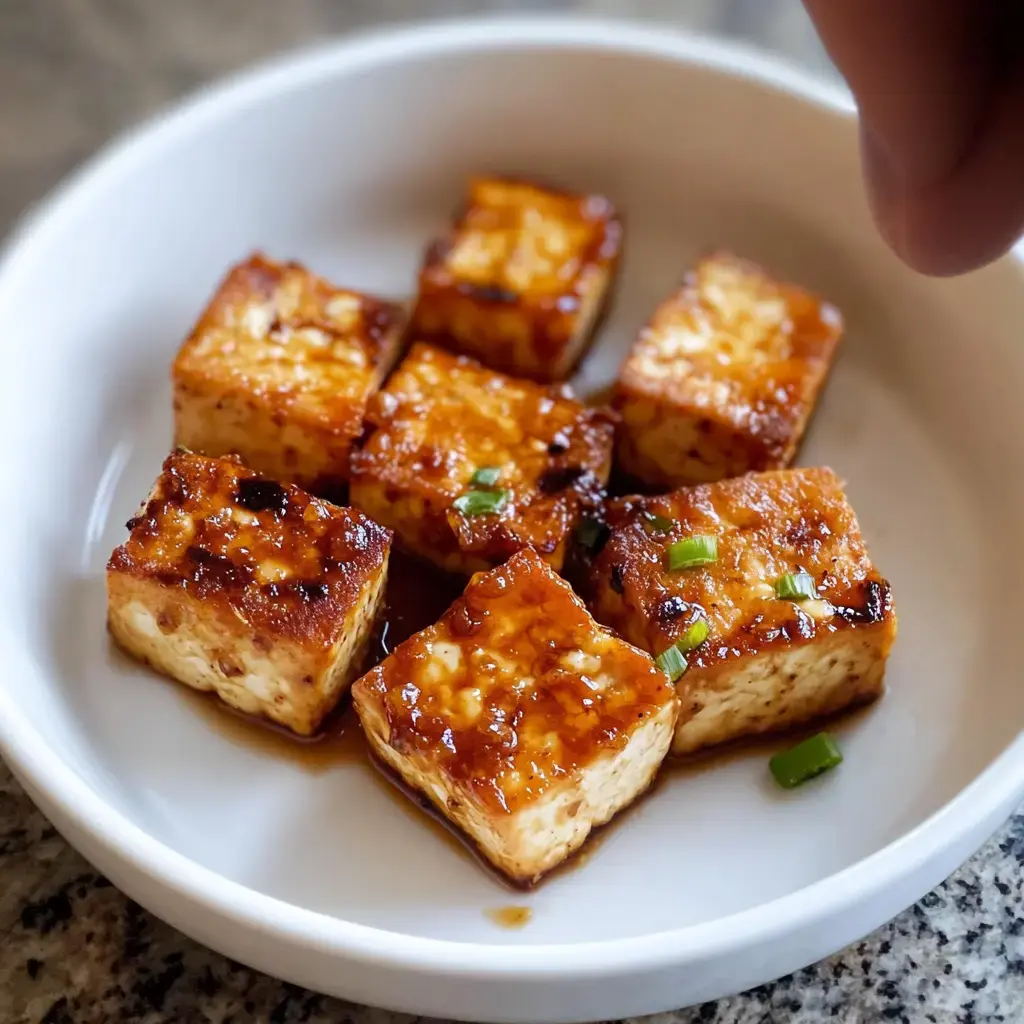 A plate of sautéed tofu cubes garnished with green onions and coated in a flavorful sauce.