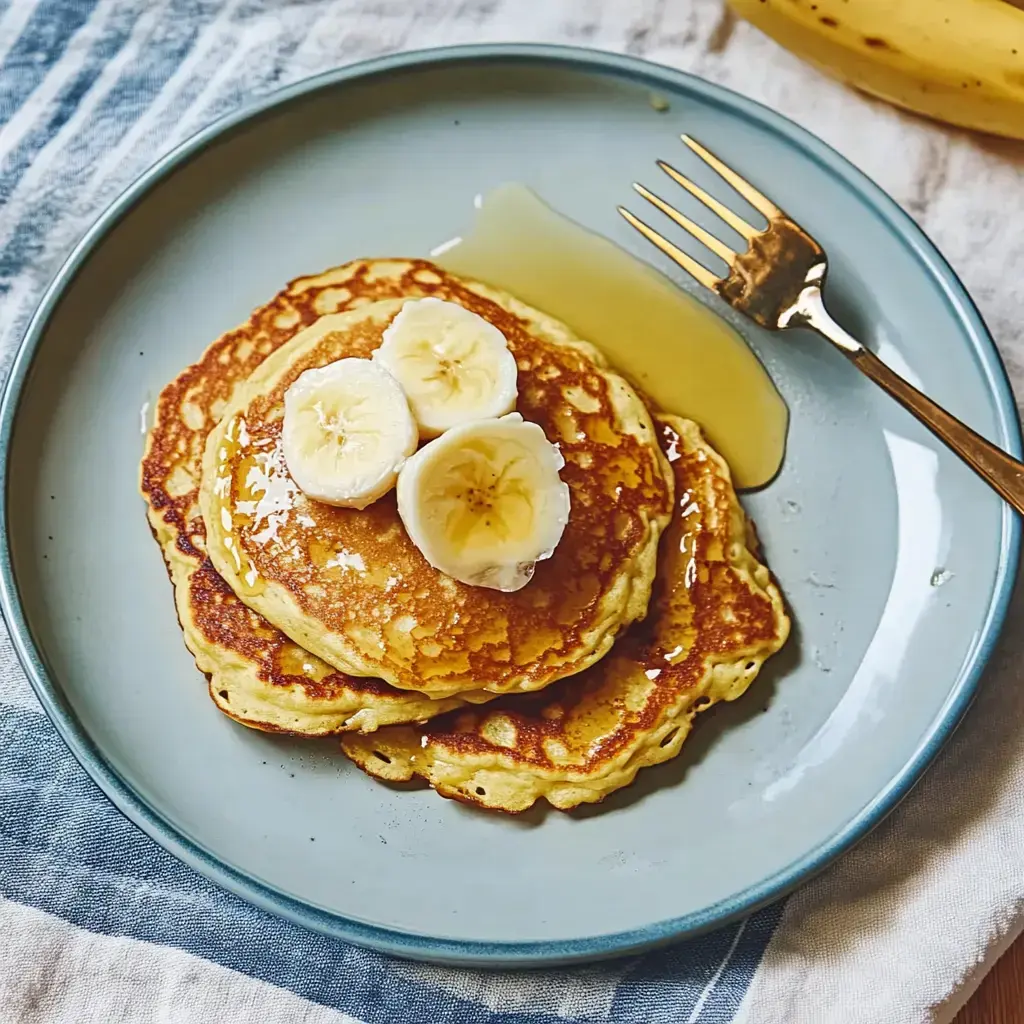 A stack of pancakes topped with banana slices and drizzled with syrup, served on a blue plate.