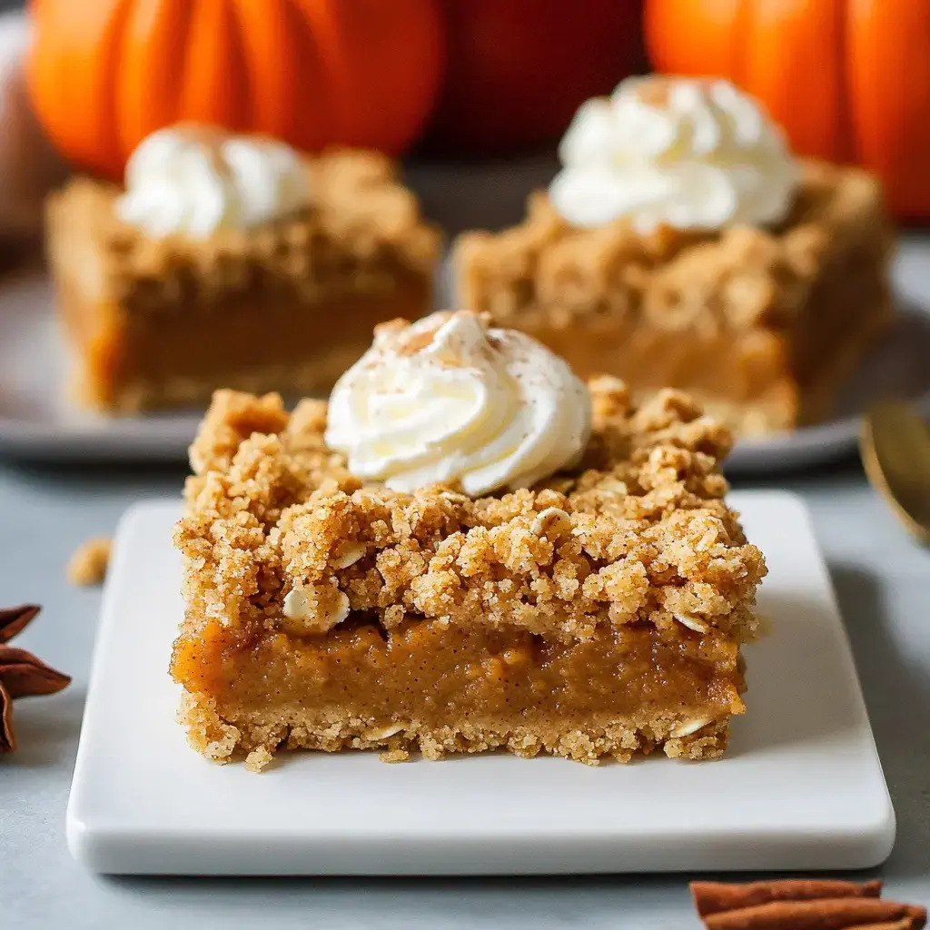 A slice of pumpkin dessert topped with whipped cream sits on a white plate, with decorative pumpkins in the background.