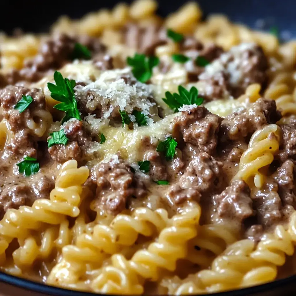 A close-up of creamy fusilli pasta topped with ground beef, parsley, and grated cheese.