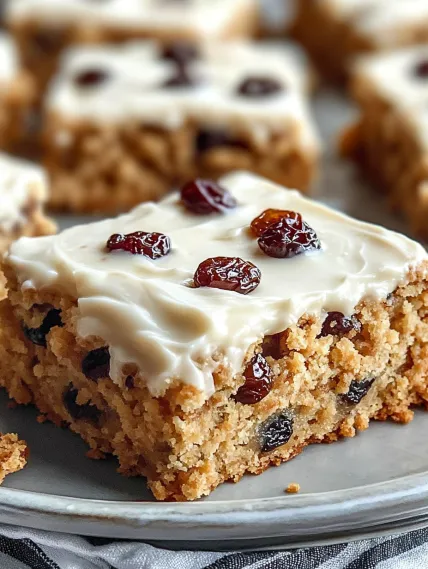 A piece of cake with white frosting and raisins.