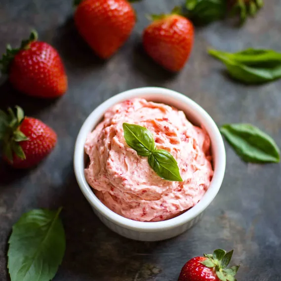 A bowl of strawberry jam with a green leaf on top.