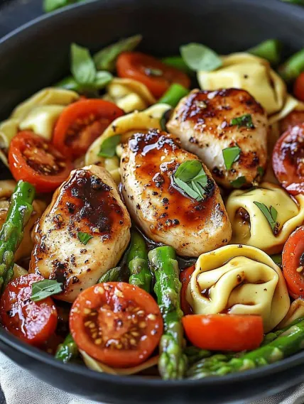 A bowl of food with chicken, tomatoes, and asparagus.