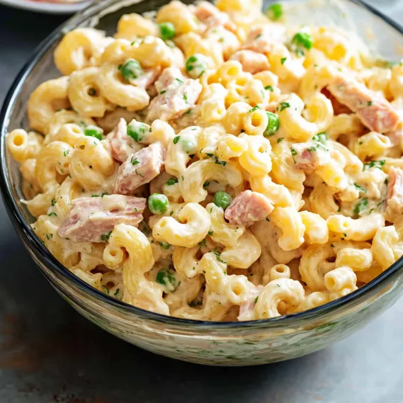 A bowl of pasta with peas and ham.