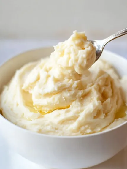 A spoon is in a bowl of mashed potatoes.