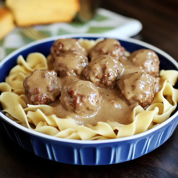 A bowl of pasta with meatballs and gravy.