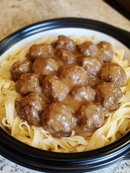 A bowl of pasta with meatballs and gravy.