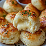 A close-up of golden-brown cheese-filled biscuits garnished with parsley, with a side of marinara sauce.