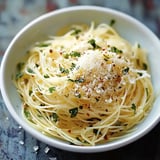 A bowl of pasta topped with grated cheese, herbs, and red pepper flakes.