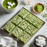 A platter of green matcha rice crispy treats topped with marshmallows, accompanied by a bowl of green matcha and a small dish of marshmallows.