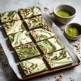 A tray of beautifully swirled chocolate bars topped with green matcha and crispy toppings, accompanied by small bowls of matcha powder.