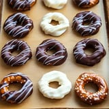 A tray of assorted donuts featuring chocolate and white icing, some drizzled with icing and topped with sprinkles.