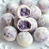 A close-up of white chocolate-coated truffles with a purple filling, displayed on a decorative plate.