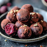 A close-up of chocolate truffles dusted with cocoa powder and topped with slivered nuts, with one truffle showing a vibrant red interior.