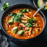 A bowl of chicken soup garnished with cilantro, diced avocado, and pieces of tortilla.