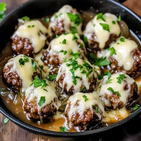 A skillet filled with meatballs topped with melted cheese and garnished with fresh parsley.